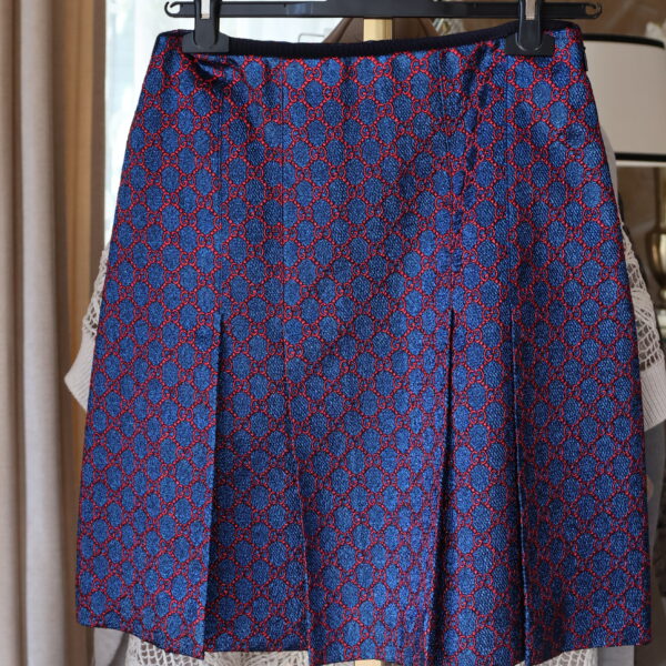 Niebieska, lekko połyskująca spódnica Gucci o linii A, ozdobiona czerwonym wzorem monogramu GG i głębokimi zakładkami, wisząca na czarnym wieszaku
