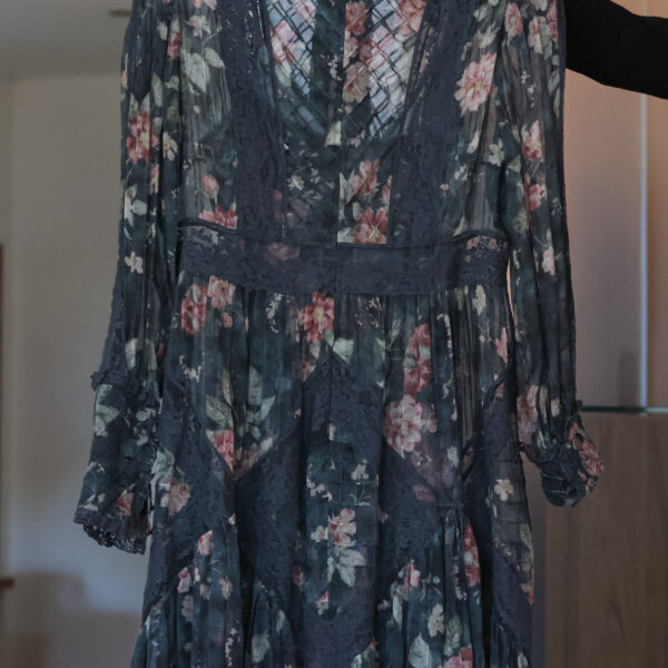 Ciemnoszara, zwiewna sukienka Zimmermann w różowe kwiaty, z długimi rękawami, stójką i bogatymi wstawkami z ciemnej koronki, wisząca na białym wieszaku