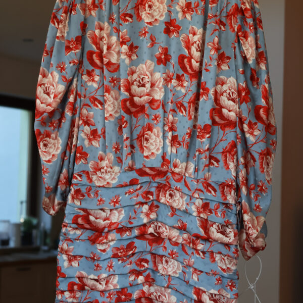 Błękitna jedwabna sukienka Magda Butrym w duże czerwone kwiaty, z długim rękawem, wycięciem na dekolcie i mocno marszczonym dołem, wisząca na wieszaku z metką