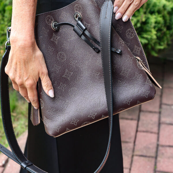 Ciemnobrązowa torebka typu worek Louis Vuitton Muria ze skóry Mahina z perforowanym wzorem Monogram, trzymana przez kobietę w czarnym stroju