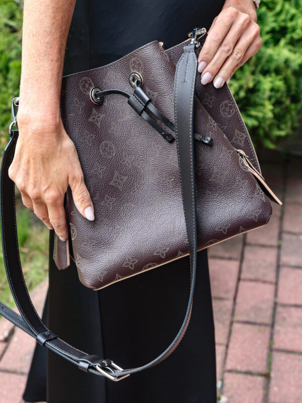 Ciemnobrązowa torebka typu worek Louis Vuitton Muria ze skóry Mahina z perforowanym wzorem Monogram, trzymana przez kobietę w czarnym stroju