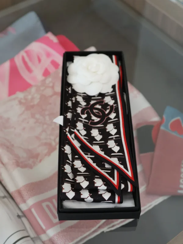 Czarno-biały jedwabny Chanel Twilly z logo CC i czerwonym obszyciem w czarnym pudełku z białą kamelią.