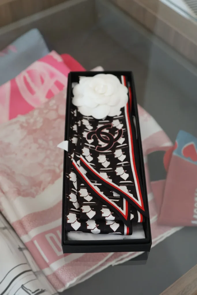 Czarno-biały jedwabny Chanel Twilly z logo CC i czerwonym obszyciem w czarnym pudełku z białą kamelią.
