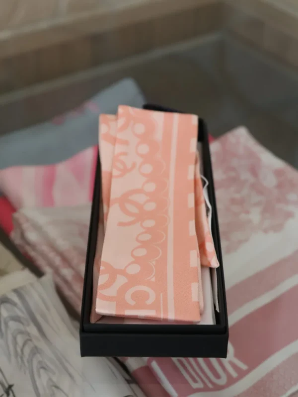 Różowy jedwabny Chanel Twilly z logo CC ułożony w czarnym pudełku Chanel.