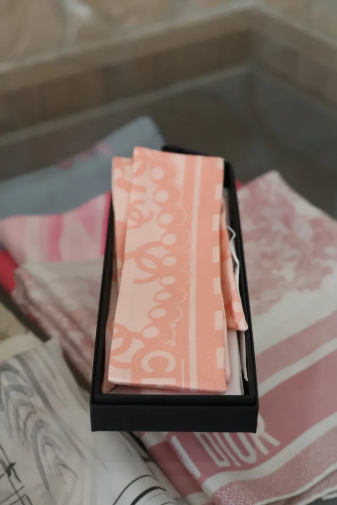 Różowy jedwabny Chanel Twilly z logo CC ułożony w czarnym pudełku Chanel.