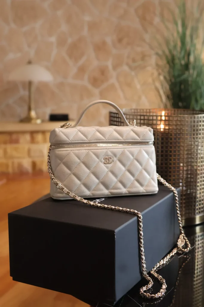 Szara pikowana torebka Chanel Vanity Case z logo CC, łańcuszkiem i rączką, na pudełku Chanel