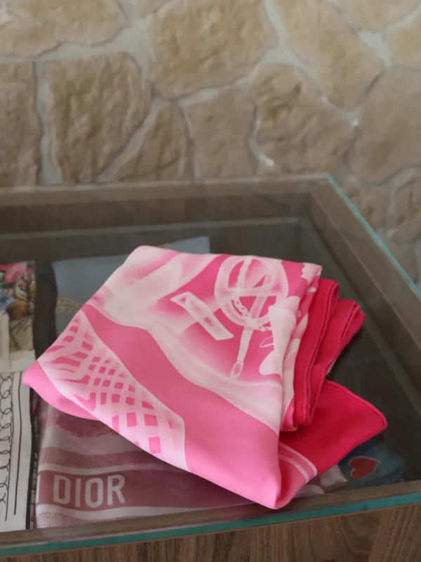 Różowa jedwabna chusta Hermès złożona na szklanym stoliku.