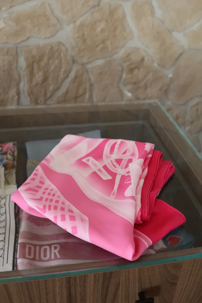 Różowa jedwabna chusta Hermès złożona na szklanym stoliku.